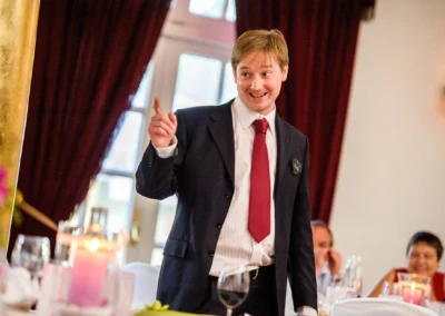 Best man in Anzug haelt Rede bei Hochzeitsfeier im Kurhaus Bad Toelz, daneben Kerzen und Gaeste, Hochzeitsreportage.