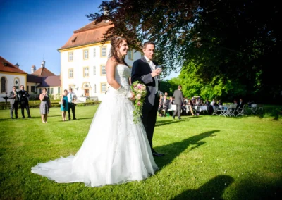 Brautpaar im Garten von Schloss Aufhausen bei einer Hochzeit. Gäste im Hintergrund. Hochzeitsfotograf in Oberbayern.