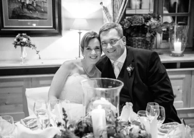 Brautpaar laechelt am Tisch mit Kerze und Gedecken bei Hochzeitsfeier. Hochzeitsfotografie im Brauereigasthof Aying.