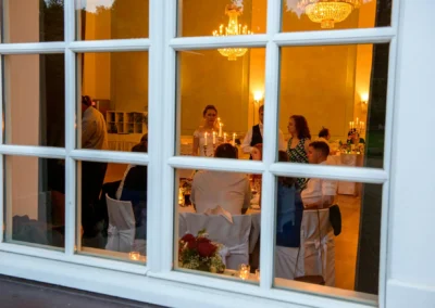 Gäste bei einer Hochzeitsfeier in der Orangerie Ansbach, fotografiert durch ein Fenster. Hochzeitsreportage.