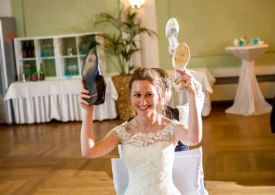 Braut hebt Schuhe beim Hochzeitsspiel in der Orangerie Ansbach. Hochzeitsfotografie mit fröhlicher Stimmung.