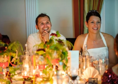 Brautpaar lacht am Tisch, beleuchtet von Kerzenlicht, bei ihrer Hochzeitsfeier. Hochzeitsfoto in Hotel am Langwieder See.