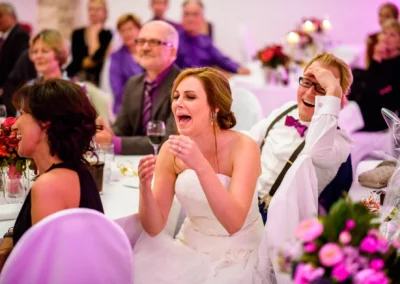 Lachende Gaeste bei einer Hochzeit in Pfettrach, Braut und Gruppe lachen bei der Hochzeitsreportage.