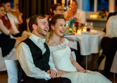 Hochzeitsreportage in Ansbach: lachendes Brautpaar bei einer Hochzeit, im Hintergrund feiernde Gaeste.