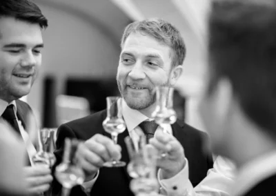 Hochzeitsfoto in Pfettrach: Gruppe von Maennern beim Anstossen mit Glaesern, fröhliche Szene in eleganter Kleidung.
