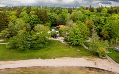 Eine Hochzeitsgesellschaft hat sich vor einem Gebäude im Wald nahe eines Strandes versammelt. Fotografiert von einem Hochzeitsfotografen am Starnberger See.