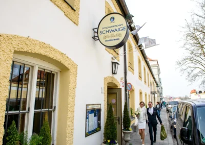 Brautpaar verlässt Schlosswirtschaft Schwaige in München-Nymphenburg nach Hochzeit. Hochzeitsfoto von Außenaufnahme.