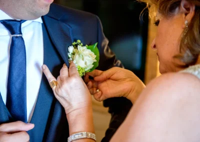 Eine Frau befestigt einen Blumenanstecker an den Anzug eines Mannes. Sie trägt Schmuck.