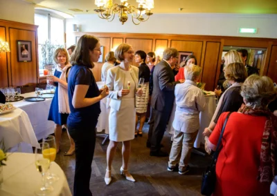 Gäste bei Hochzeitsfeier in München-Nymphenburg, elegant gekleidet, bei Gesprächen und Getränken im Festsaal.