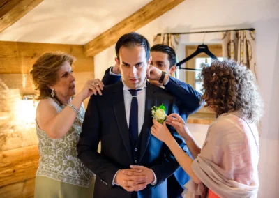 Ein Bräutigam im Anzug wird von drei Personen für die Hochzeit vorbereitet.