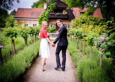 Brautpaar Hand in Hand vor einem Haus in Gartenanlage beim Künstlerhaus Gasteiger, Hochzeit bei Landsberg-Lech.