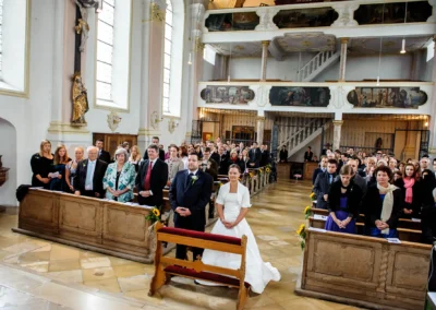 Braut und Bräutigam knien in einer vollen Kirche in Zorneding, flankiert von Gästen in festlicher Kleidung.