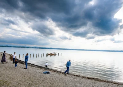 Menschen am Ufer des Starnberger Sees bei einer Hochzeitsreportage, im Hintergrund Wolken und ein Boot.