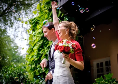 Lachendes Brautpaar mit Blumenstrauss, umgeben von Seifenblasen. Hochzeitsfotografie im Kuenstlerhaus Gasteiger am Ammersee.