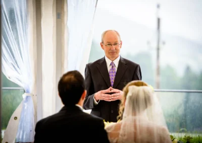 Ein Mann in einem Anzug spricht vor einem Brautpaar. Die Braut trägt einen Schleier. Zeremonie im festlichen Ambiente.