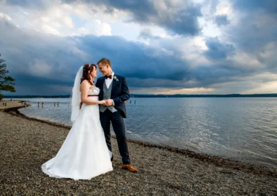 Brautpaar steht am Ufer des Starnberger Sees während ihrer Hochzeitsreportage in der Gemeinde Münsing.
