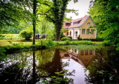 Hochzeitsfoto mit Haus und Teich bei Hochzeit im Kuenstlerhaus Gasteiger, westlich von Muenchen.