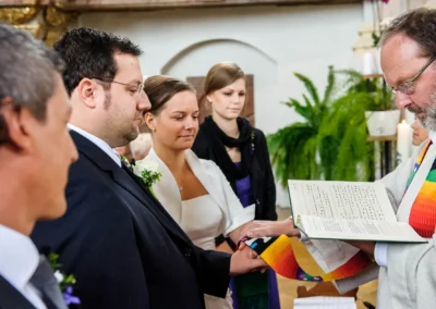 Ein Brautpaar steht Hand in Hand mit einem Geistlichen, der ein Buch liest; feierlicher Moment in der Kirche.
