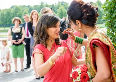 Zwei Frauen in festlicher Kleidung lachen bei einer Hochzeit in Schleissheim, umgeben von Gaesten im Freien.
