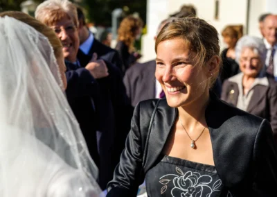 Lächelnde Frau in eleganter Kleidung bei einer Hochzeitsfeier in Kirchheim, Sonnenlicht im Hintergrund.