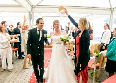 Das Brautpaar geht strahlend durch einen Blütentunnel, umgeben von jubelnden Gästen in einem festlich dekorierten Zelt.