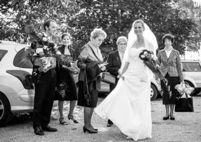 Braut laechelt beim Empfang auf einer Hochzeit in Taufkirchen bei Muenchen, umgeben von Gaesten mit Blumen.