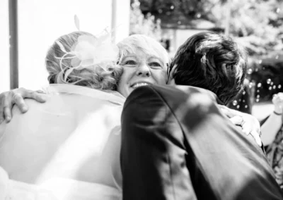 Ein freudiges Gesicht wird innig zwischen Braut in Schleier und Anzugträger umarmt, Seifenblasen schweben im Hintergrund.