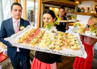 Eine Gruppe serviert kunstvoll angerichtete Canapés. Ein Mann im Anzug hält ein Tablett, Frauen tragen Dirndl.