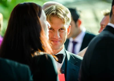 Mann in Anzug laechelt bei einer Hochzeitsreportage in Taufkirchen, umgeben von Gaesten.