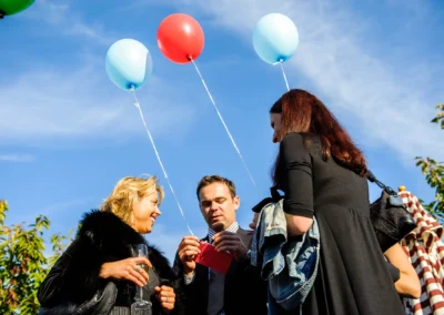 Hochzeitsfoto in Taufkirchen: Menschen halten bunte Ballons bei einer Feier unter blauem Himmel.