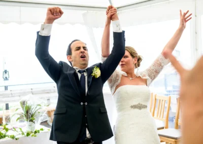 Ein Brautpaar jubelt mit erhobenen Armen, der Bräutigam im dunklen Anzug, die Braut im Spitzenkleid.