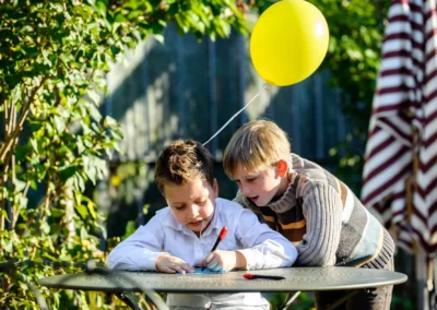 Zwei Kinder zeichnen bei einer Hochzeit in Taufkirchen bei Muenchen. Hochzeitsfoto im Freien mit gelbem Ballon.