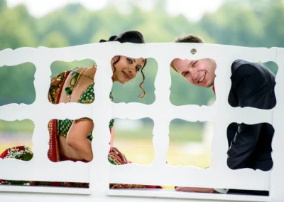Brautpaar laechelt durch Gartenzaun bei Hochzeit im Schlosspark Schleissheim, Hochzeitsfotografie nördlich Muenchen.