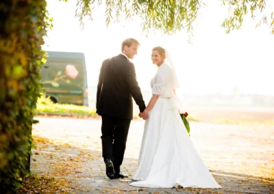 Brautpaar bei Hochzeitsportraits in Taufkirchen, sie halten Haende auf einem herbstlichen Weg, romantische Szene.