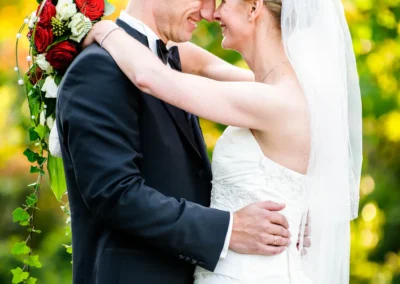Brautpaar umarmt sich in Garten, Brautstrauss mit roten Rosen, fotografiert in Taufkirchen bei einer Hochzeitsreportage.
