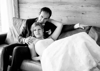 Ein Brautpaar entspannt auf einem Sofa. Sie liegt in seinem Arm, beide schauen entspannt. Hintergrund aus Holz.
