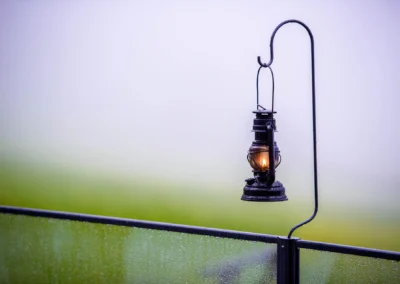 Eine Laterne an einem Haken, beleuchtet und mit Wassertropfen bedeckt, hängt über einer verregneten Glasscheibe.
