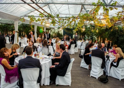 Gäste bei Hochzeitsfeier in alter Gaertnerei Taufkirchen, elegant gedeckte Tische, Kerzenlicht, Hochzeitsfotografie.