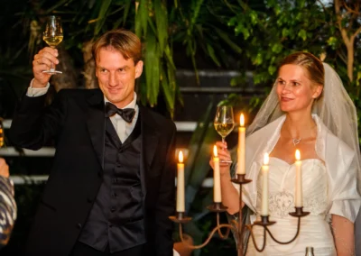 Brautpaar erhebt Gläser bei Hochzeit nahe Muenchen, festlich beleuchtet mit Kerzen im Hintergrund. Hochzeitsfotografie.