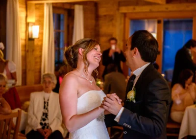 Ein Brautpaar tanzt glücklich in einer holzverkleideten Location. Die Braut trägt ein weißes Kleid, der Bräutigam einen Anzug.