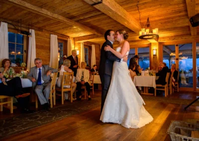 Das Brautpaar tanzt in einer rustikalen Holzstube, Gäste sitzen an Tischen, warmes Licht erzeugt eine gemütliche Atmosphäre.