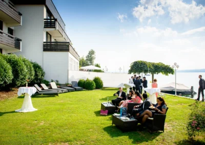 Gäste bei Hochzeit im Seehotel Leoni am Starnberger See, sitzen auf Gartenmöbeln, unterhalten sich, genießen.
