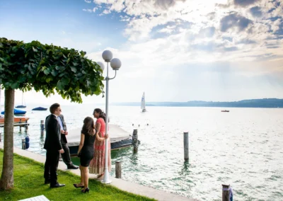 Menschen im Gespräch bei einer Hochzeit im Seehotel Leoni, mit Blick auf den Starnberger See und einem Segelboot.