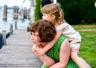 Frau mit Kind auf dem Ruecken laechelt am Steg, aufgenommen bei Hochzeitsfotografie am Starnberger See.