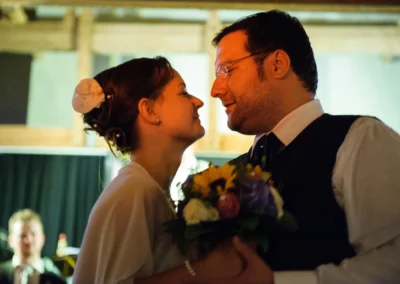 Ein Paar lächelt sich nah gegenüberstehend an. Die Frau hält einen Blumenstrauß. Beide wirken glücklich und verbunden.