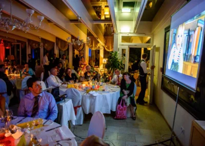 Gäste sitzen bei Hochzeitsfeier im Seehotel Leoni, Berg am Starnberger See, Video wird projiziert. Hochzeitsreportage.