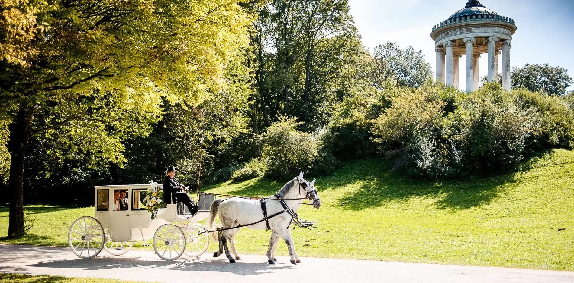 Hochzeitsfotografie einer Kutsche mit Brautpaar vor dem Monopteros im Englischen Garten in München